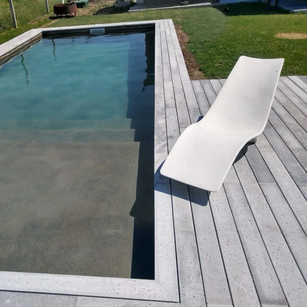 Piscina y solárium con piezas alargadas claras junto al césped